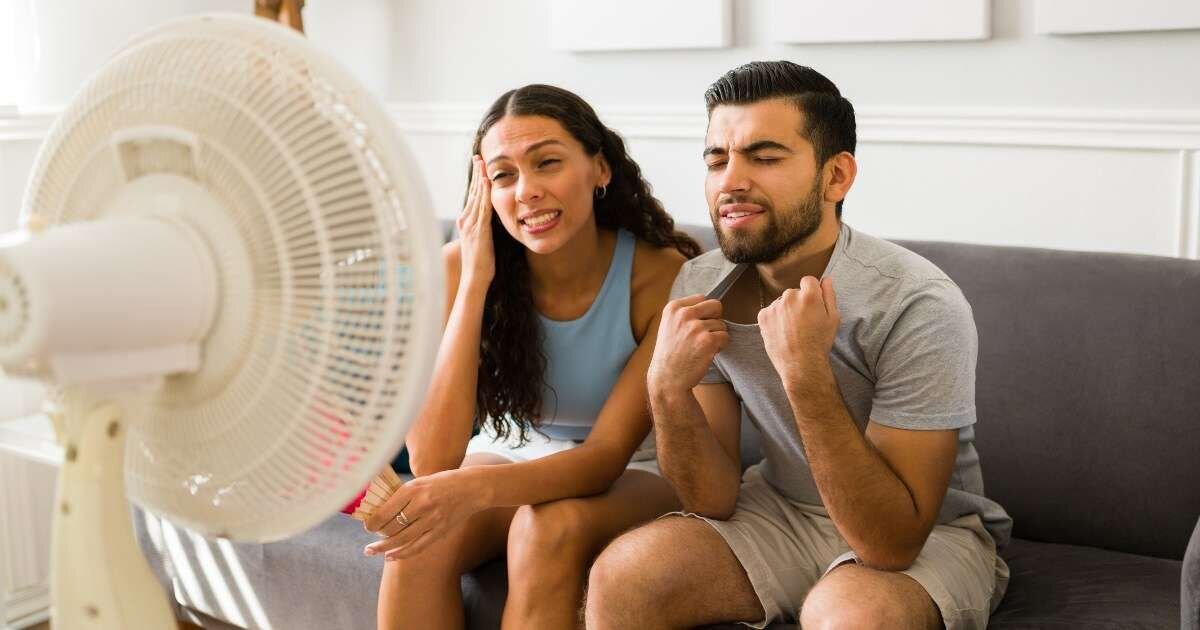 young couple sitting on couch, cooling down with a fan 