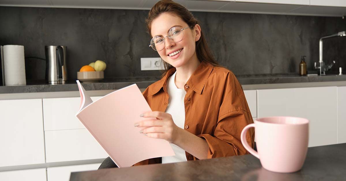 Woman smiling while sitting at kitchen island with a notebook and a coffee mug.